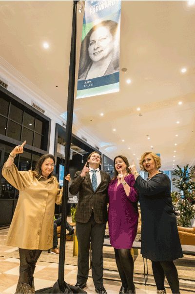 Amy Mill and friends point to a Landmarks, IL banner with her picture on it