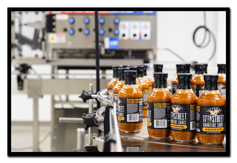 Row of bottles of 17th Street Barbecue Sauce on bottling conveyor belt.